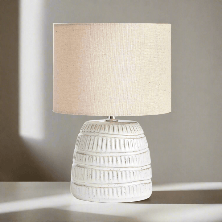 Rustic textured pottery table lamp with white glaze and linen shade, adding natural elegance to home décor.