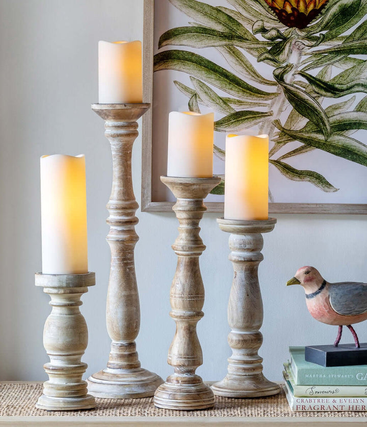 Rustic whitewashed mango wood pillar candle holders set of 2, hand-carved, standing on a table with lit candles for vintage decor.