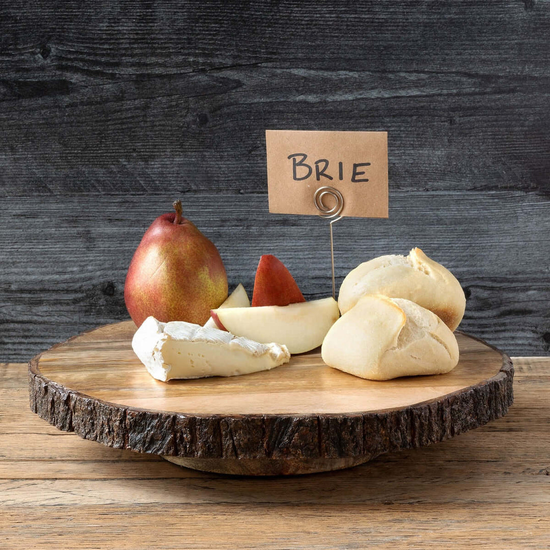 Rustic wood slice lazy Susan with bark edge displaying cheese, pears, and bread on a farmhouse table.