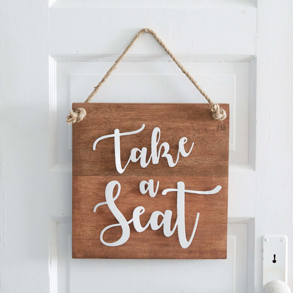 Rustic wood "Take a Seat" sign with jute rope hanging on a door, featuring playful white lettering and charm for home decor.