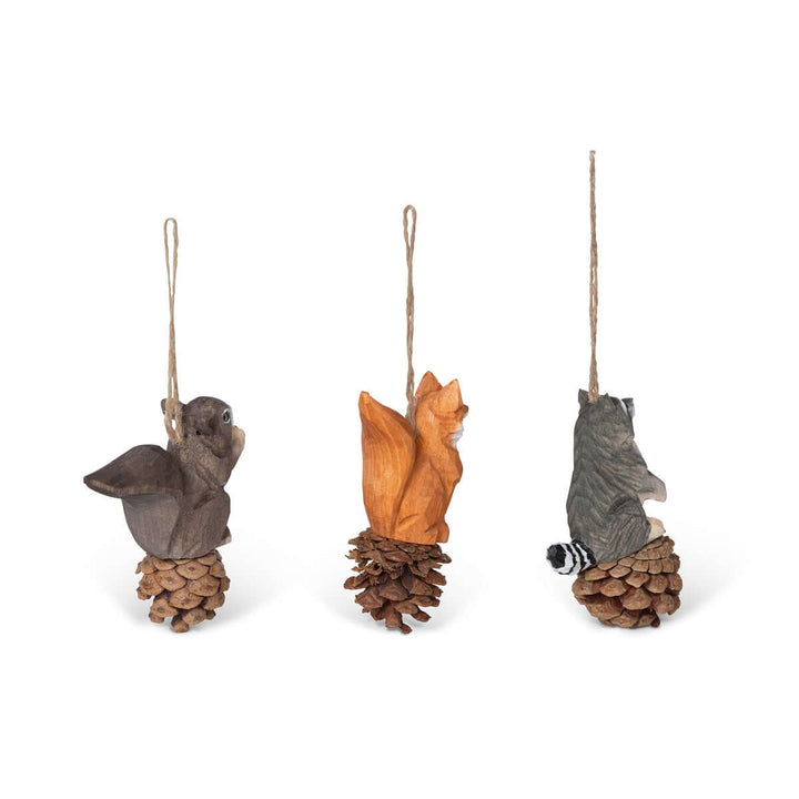 Set of 3 rustic woodland animal ornaments featuring squirrel, fox, and raccoon, hand-carved from wood on pinecones with jute strings.