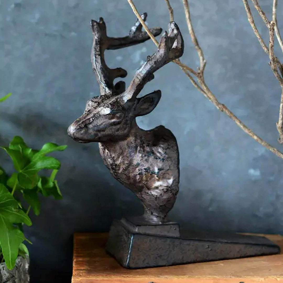 Rustic cast iron deer door stopper with antlers on wooden surface, adding woodland charm to home decor.