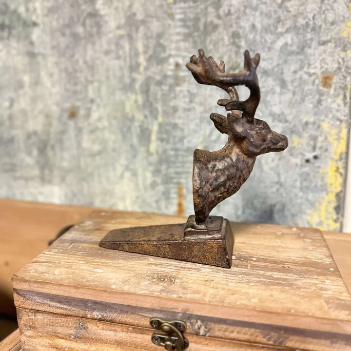 Rustic cast iron deer door stopper with antlers on a wooden base.