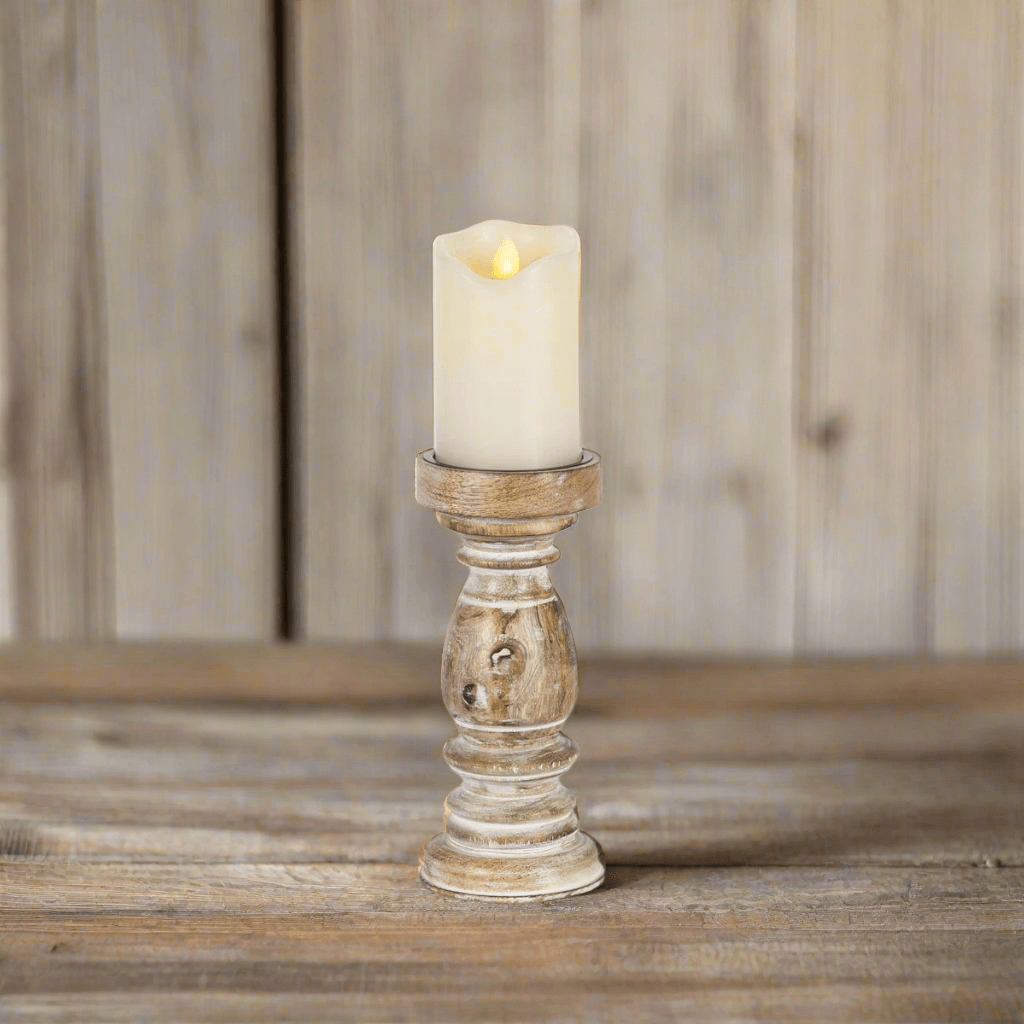 Rustic whitewashed mango wood pillar candle holder with lit candle on wooden surface