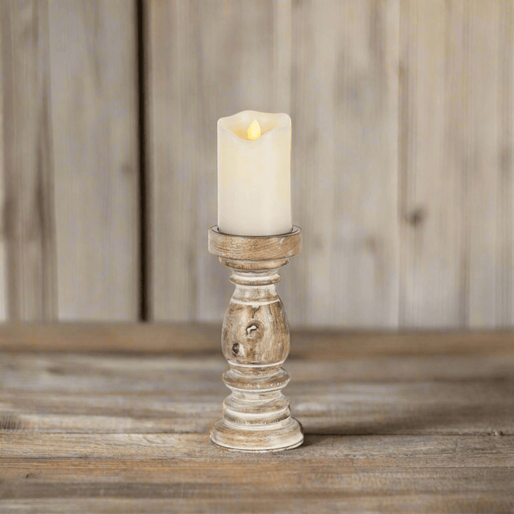 Rustic whitewashed mango wood pillar candle holder with lit candle on wooden surface