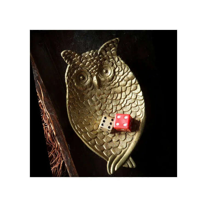 Gold owl dish with two dice on a dark wooden surface