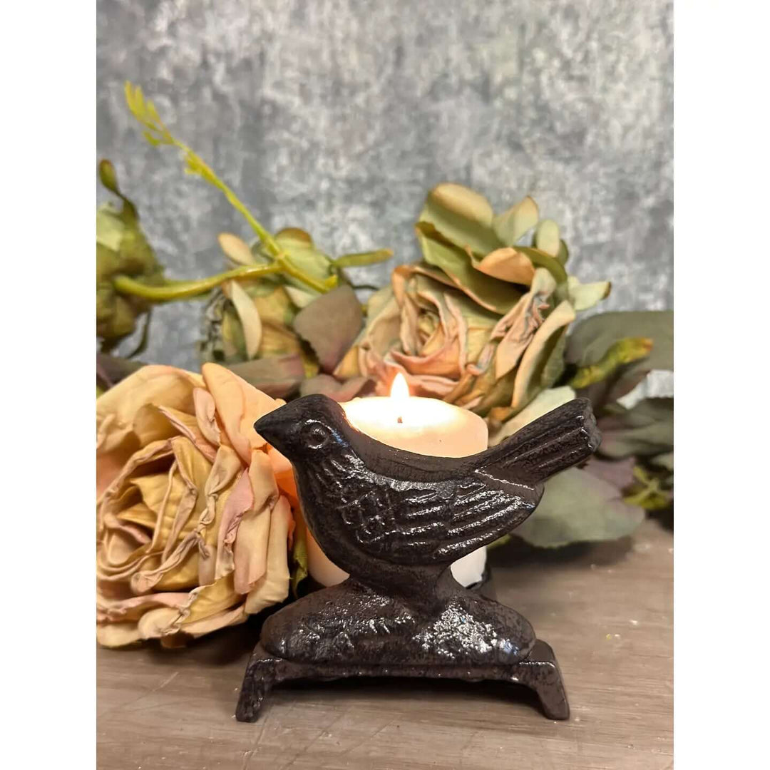 Compact metal bird candle stand with a lit candle in a romantic botanical setting