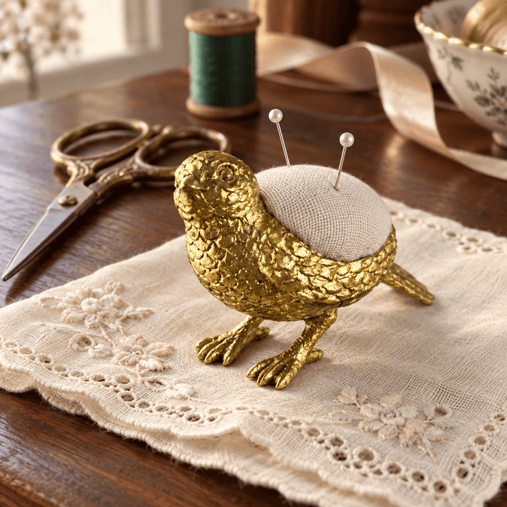 Pewter bird pincushion on an embroidered handkerchief beside scissors