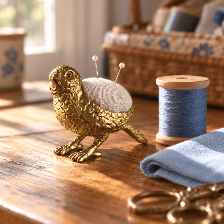 Gold-tone pewter bird pincushion on a sewing table with blue thread