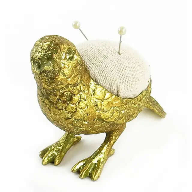 Pewter bird pincushion showing its pale fabric cushion and two pins