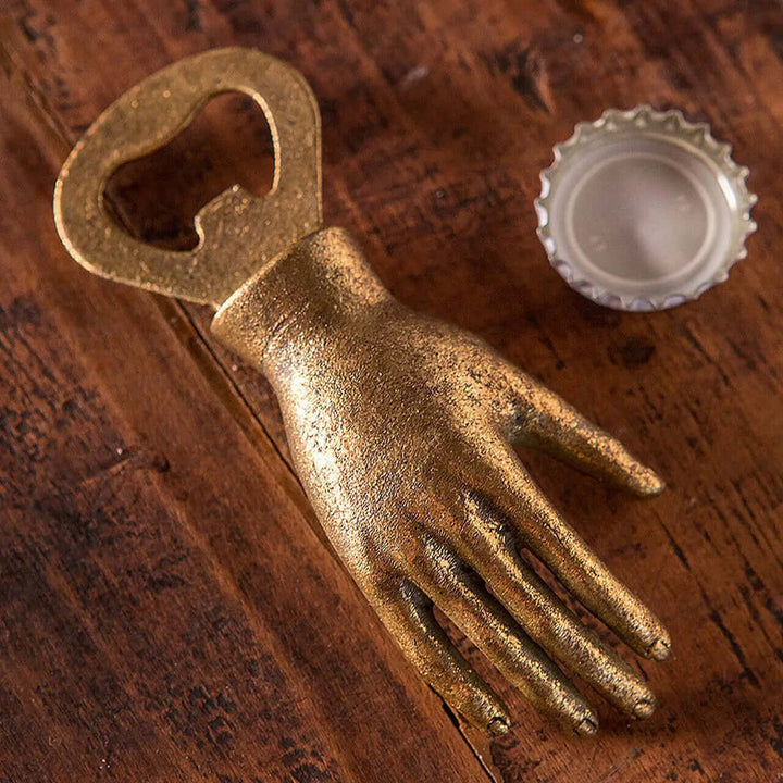 Gold-leaf iron hand bottle opener beside a crown cap on wood