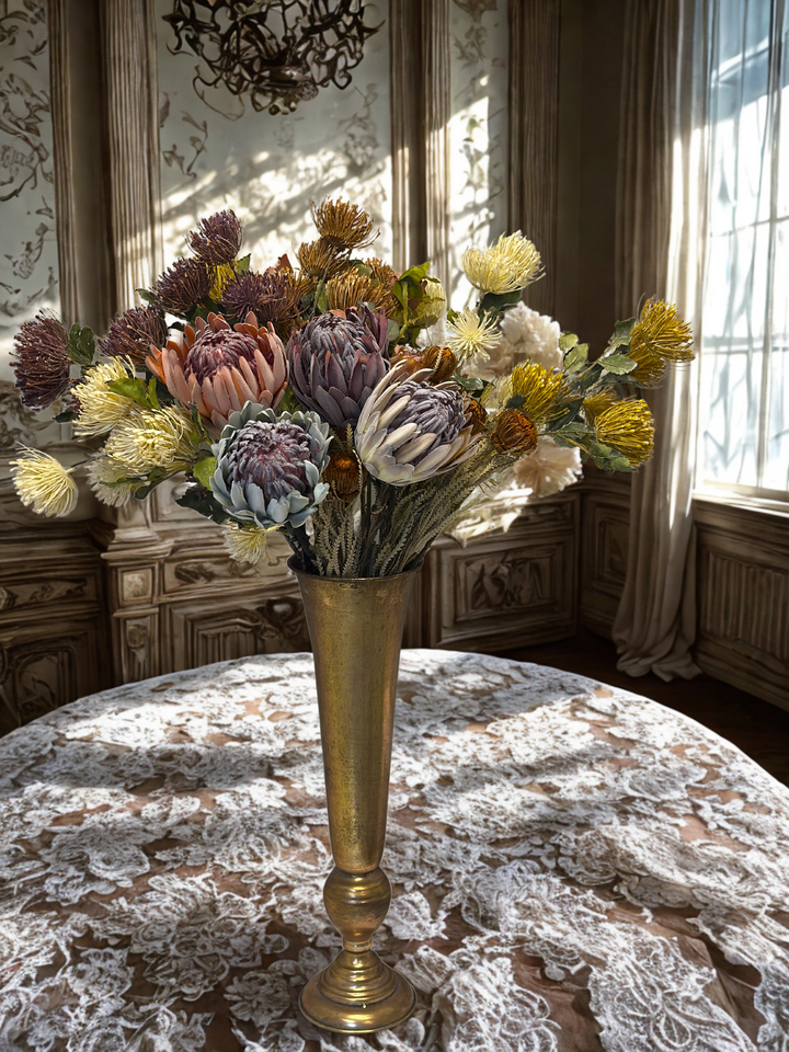 Mixed king protea faux flower stems gathered in a tall antique gold vase