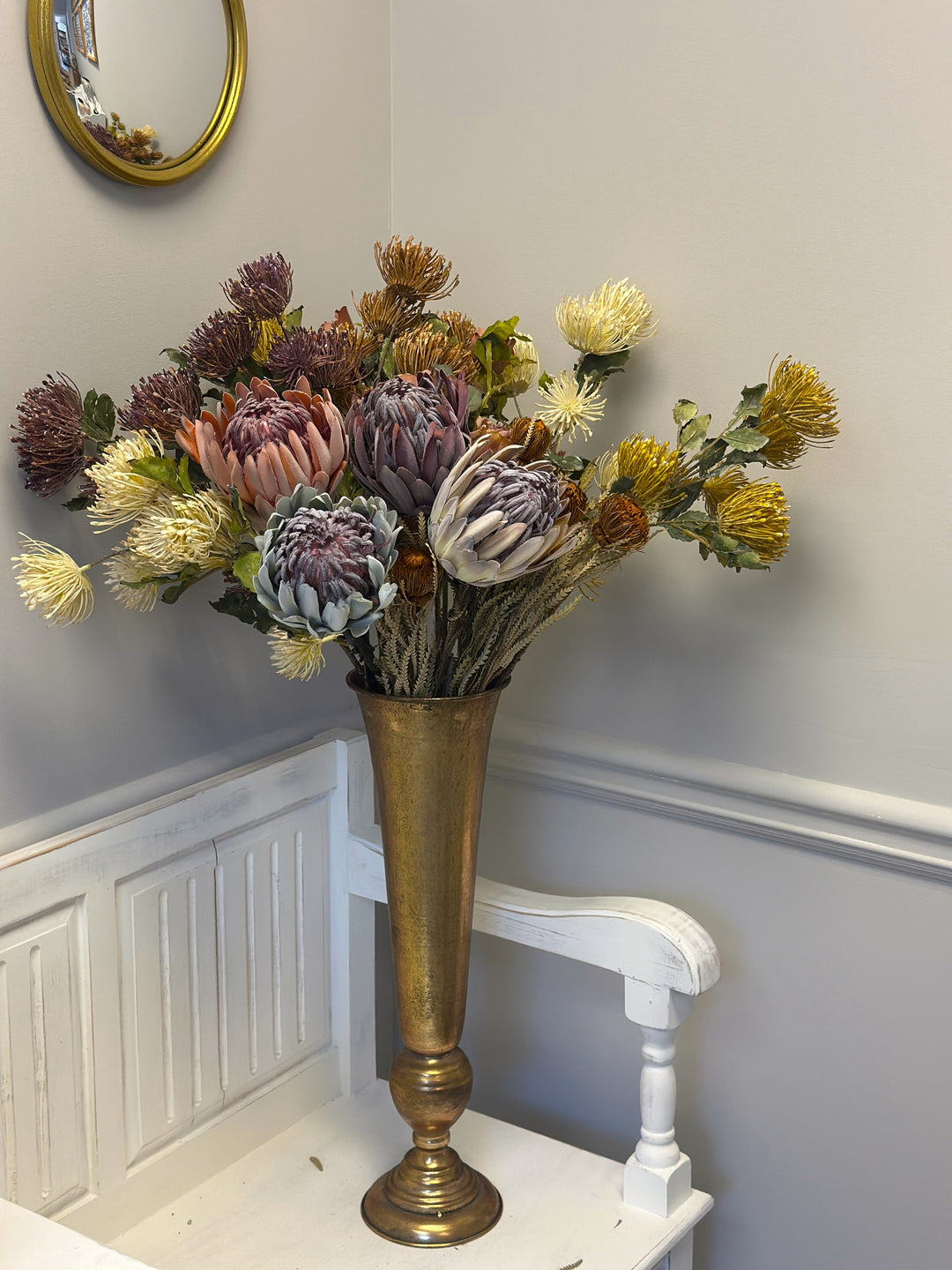 King protea stems arranged with pincushion blooms in a brass-toned floor vase