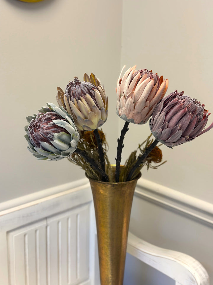 Four king protea faux flower stems displayed together in a tall gold vase