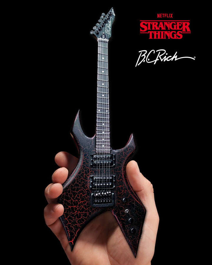 Hand holding Stranger Things Eddie’s B.C. Rich Warlock Mini Guitar Replica with Stranger Things logo in background