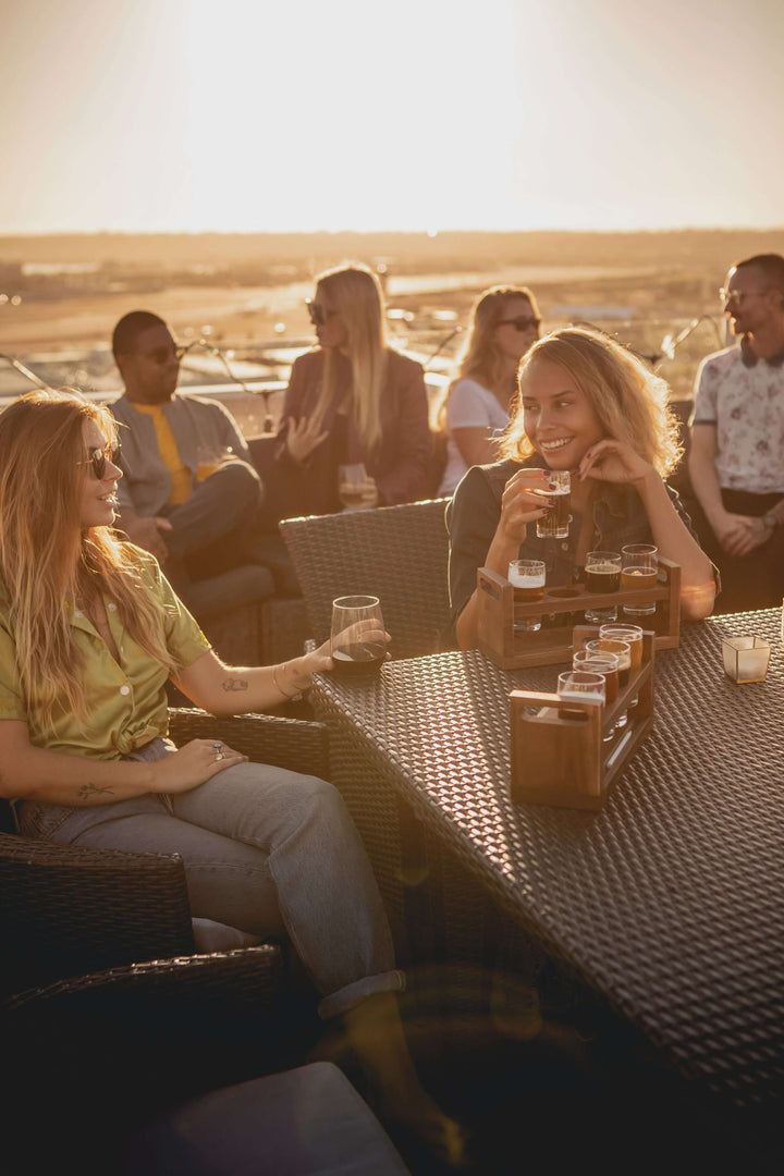 Friends enjoying an outdoor sunset gathering with a Rustic Craft Beer Flight Tasting Set on a patio.