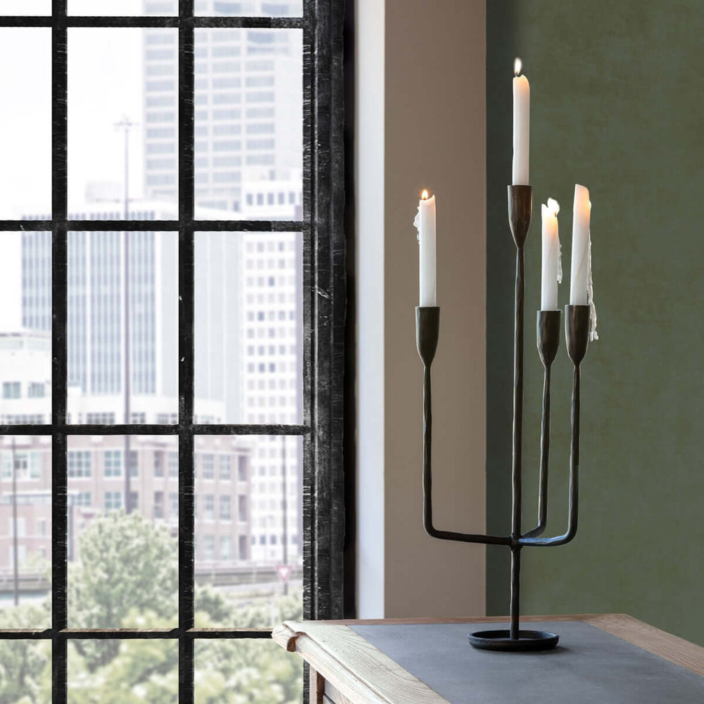 Tall Rustic Iron Candelabra on a wooden table by a window, showcasing handcrafted blacksmith design with burning candles for a rustic touch.