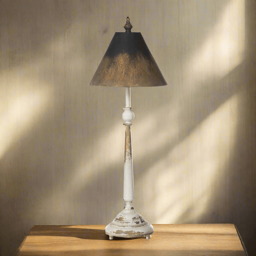 Tall vintage table lamp with distressed cream base, black and gold shade, standing on wooden table, evoking nostalgic elegance.