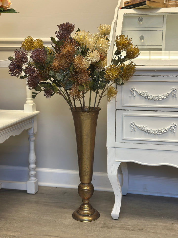 Pincushion protea arrangement in an antique gold vase beside a white chest
