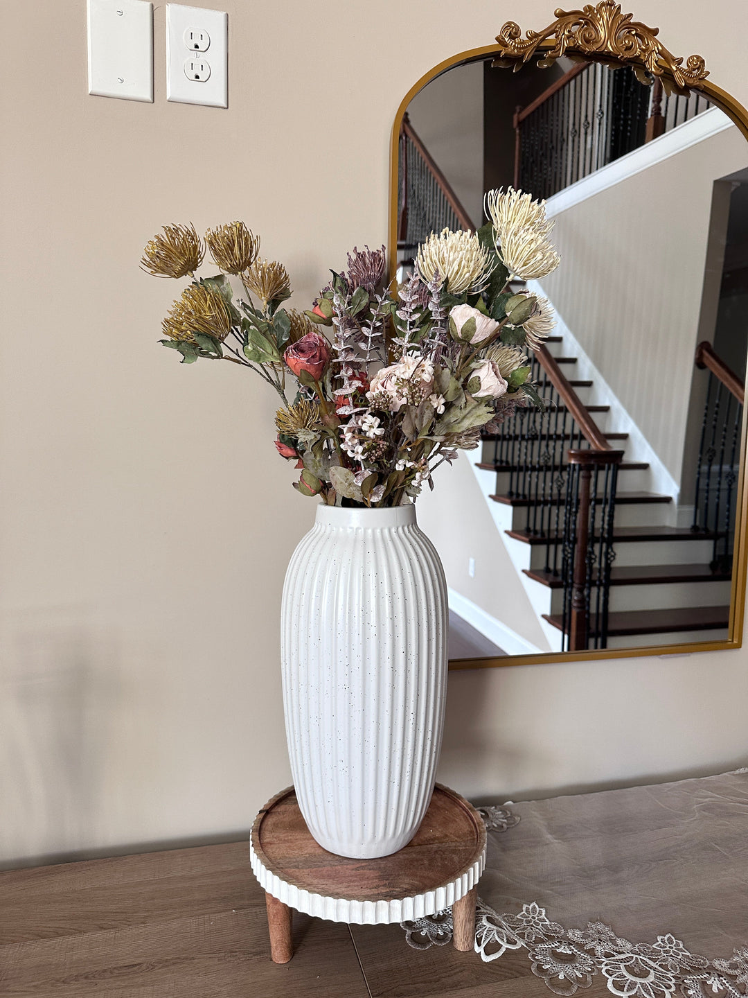White and muted protea stems arranged in a ribbed white vase beneath a mirror