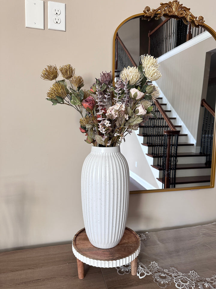 White and muted protea stems arranged in a ribbed white vase beneath a mirror