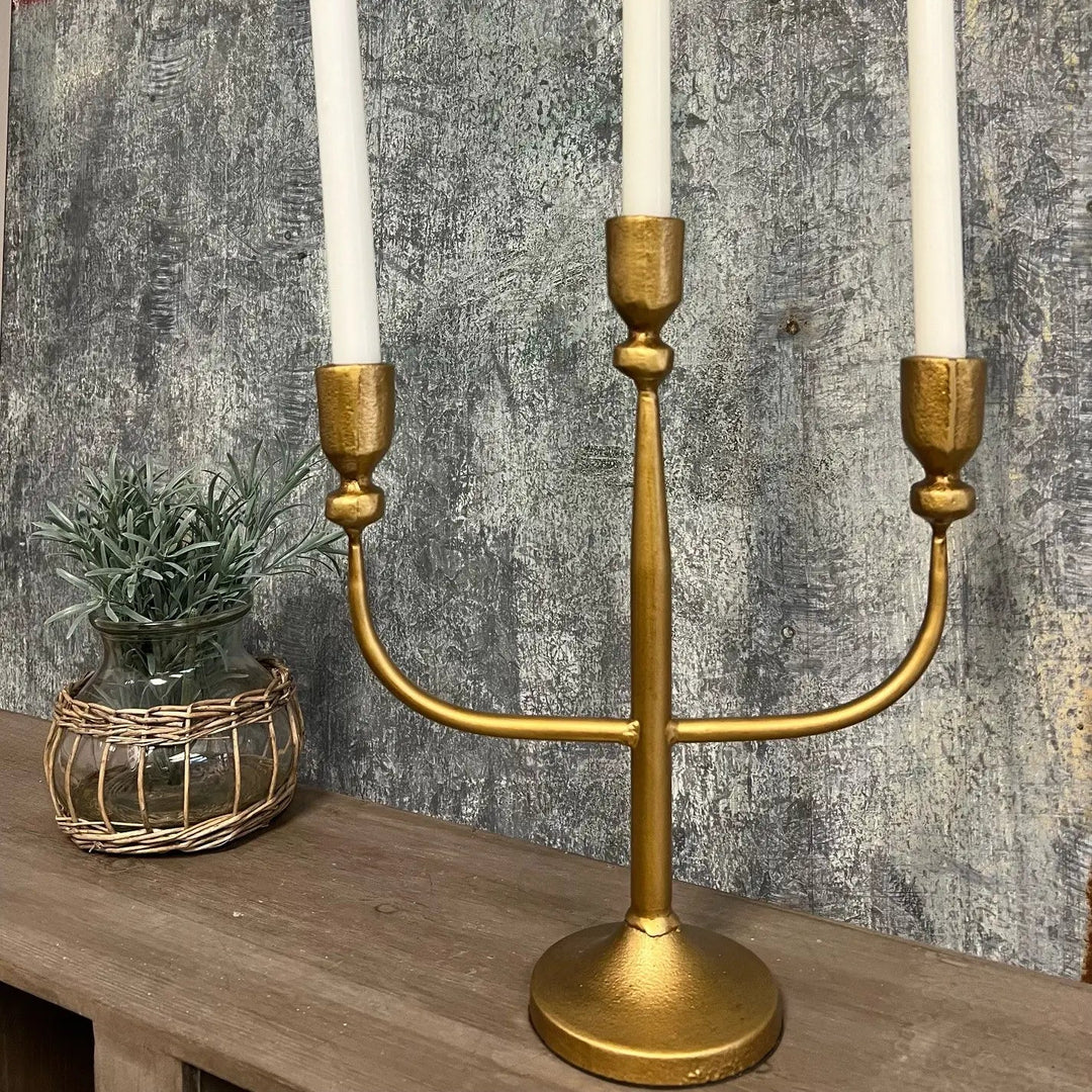 Gold three-arm candelabra with white tapers beside a small plant