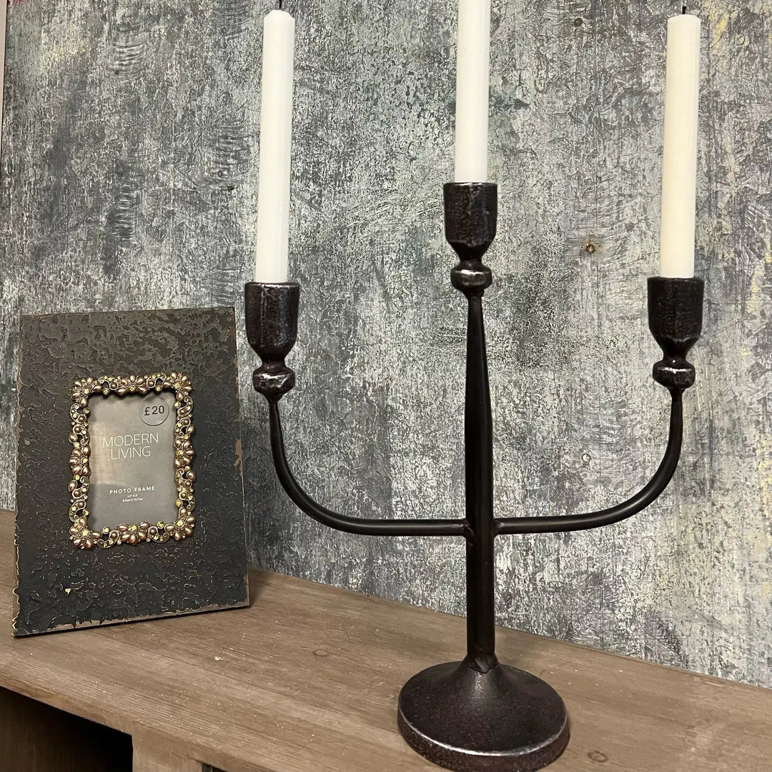 Black three-arm candelabra with white tapers beside a frame