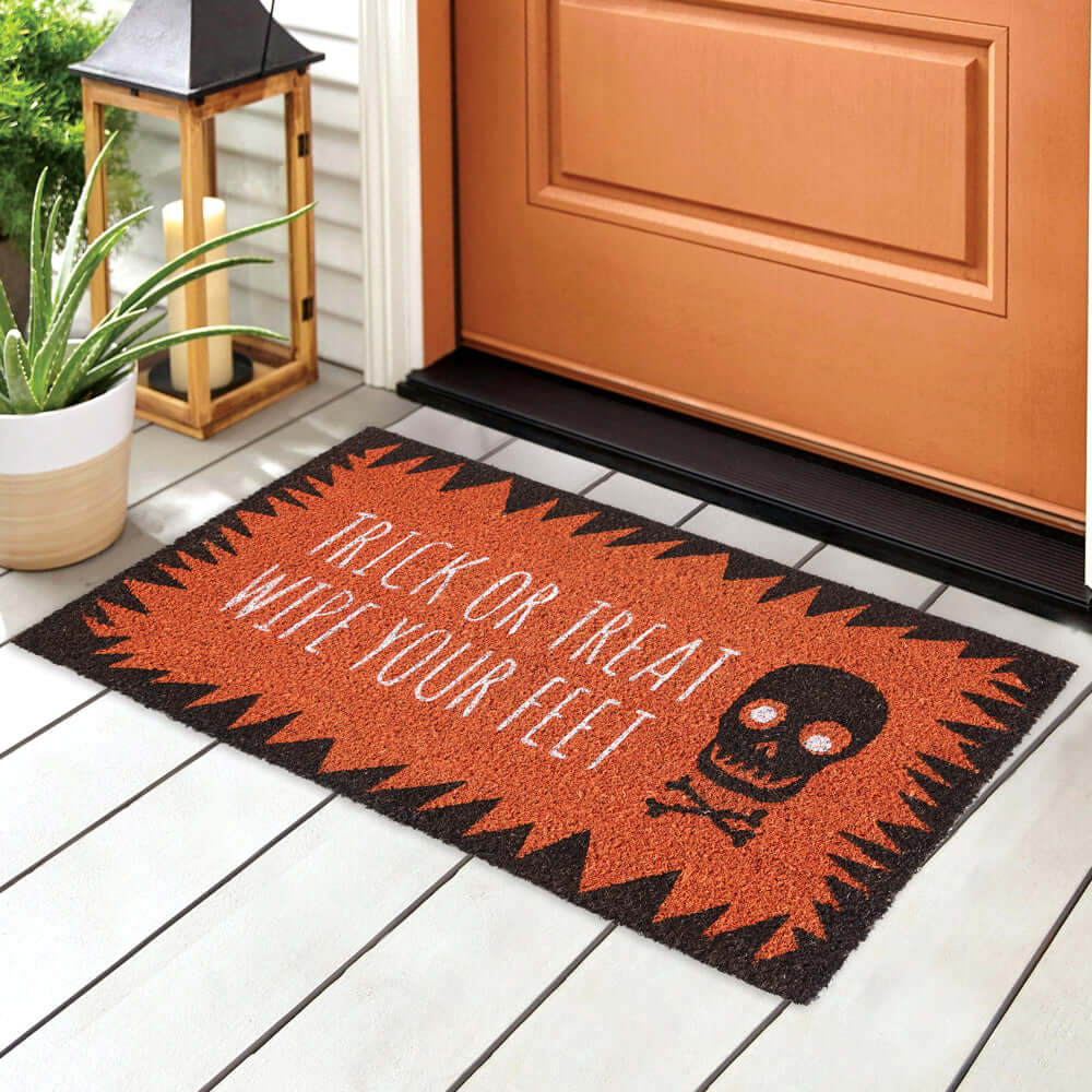 Halloween doormat with skull design at door; text reads 'Trick-or-Treat Wipe Your Feet,' orange and black colors; festive home decor.