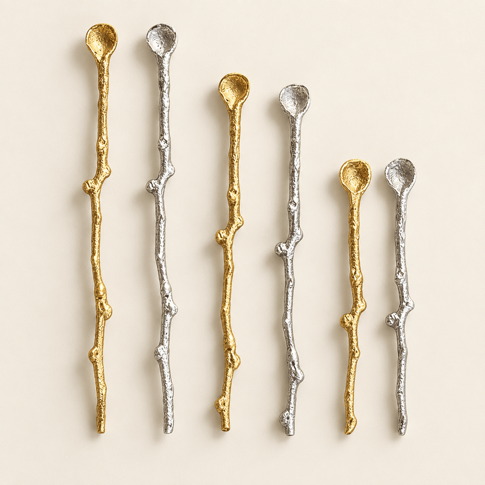 Gold and silver twig-handle decorative serving spoons arranged on an ivory studio background.