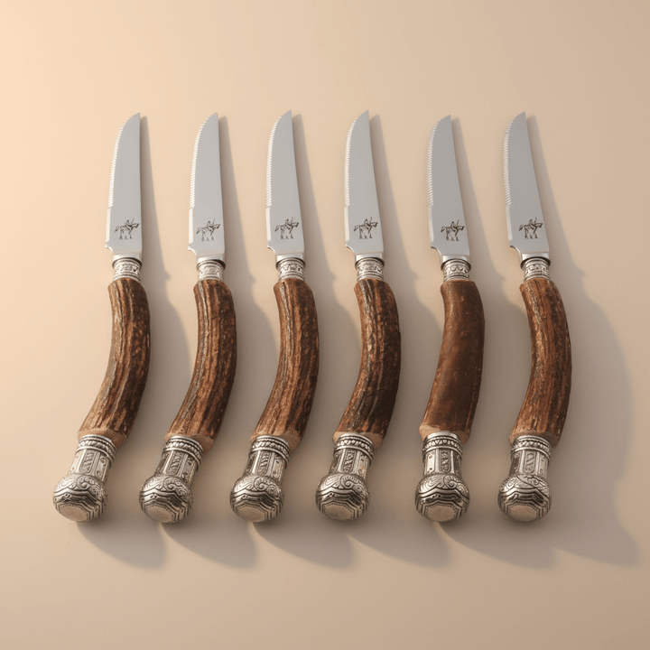 Set of six steak knives with antler handles on a beige background