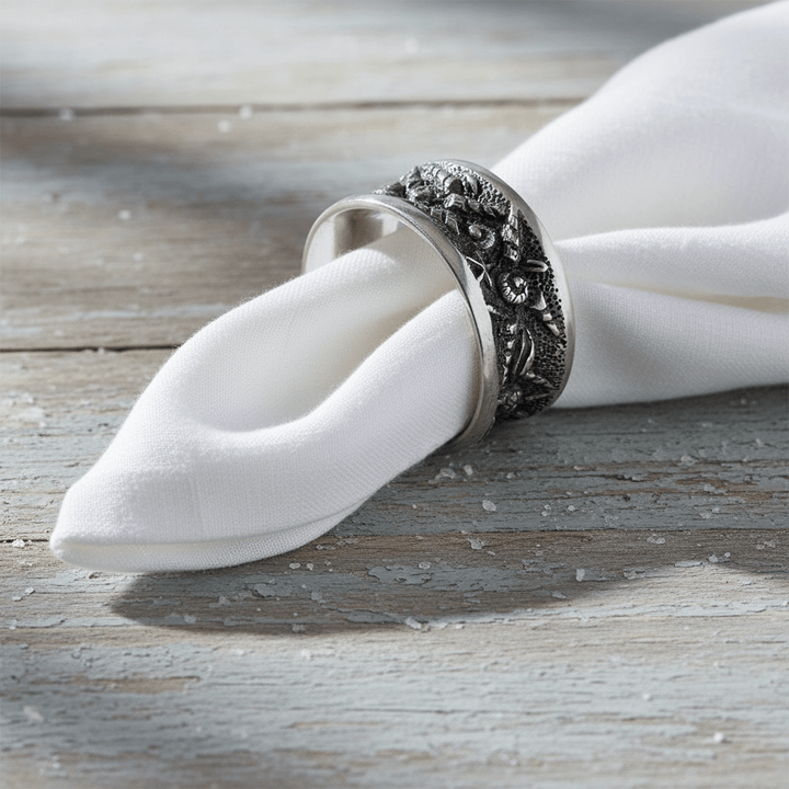Decorative silver napkin ring holding a white napkin on a wooden surface