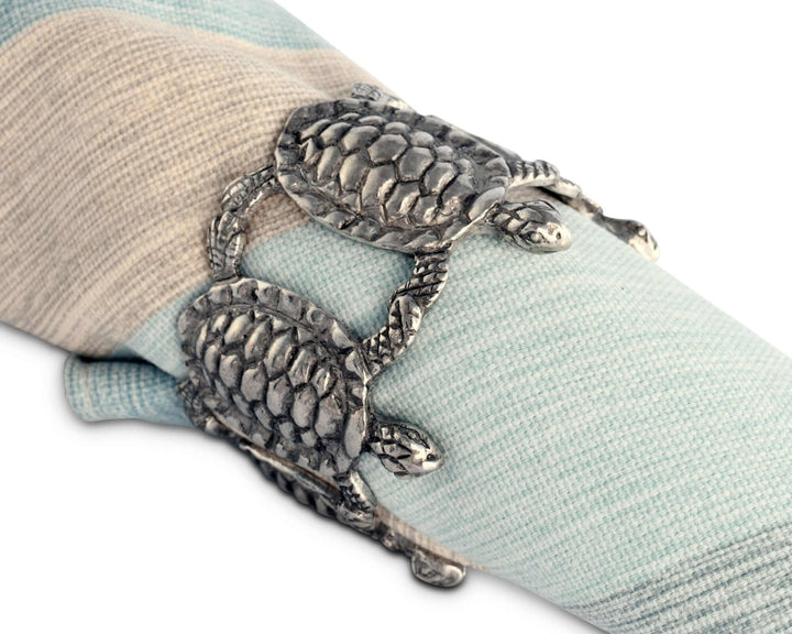 Silver turtle-shaped napkin ring on a light blue napkin with a beige fabric background