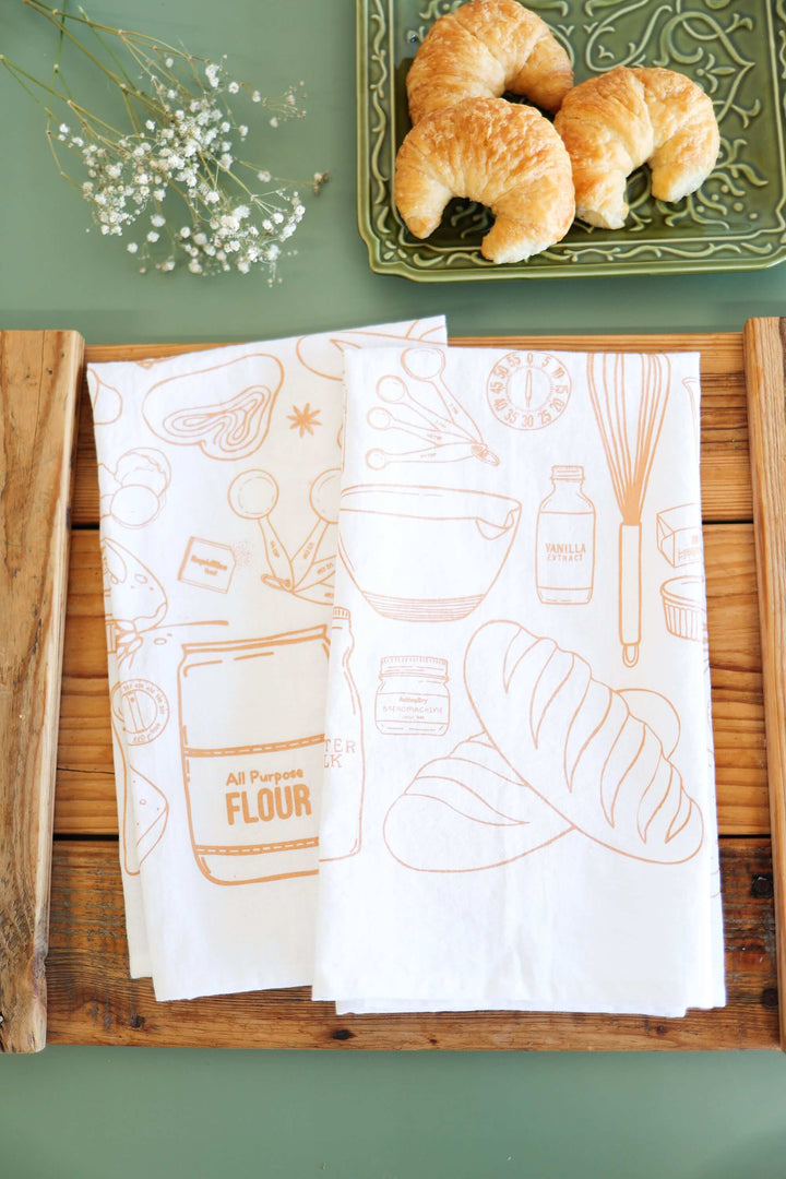 Vintage Bread Baking Tea Towel with hand-drawn illustrations, showcasing bread and baking tools on a kitchen table.