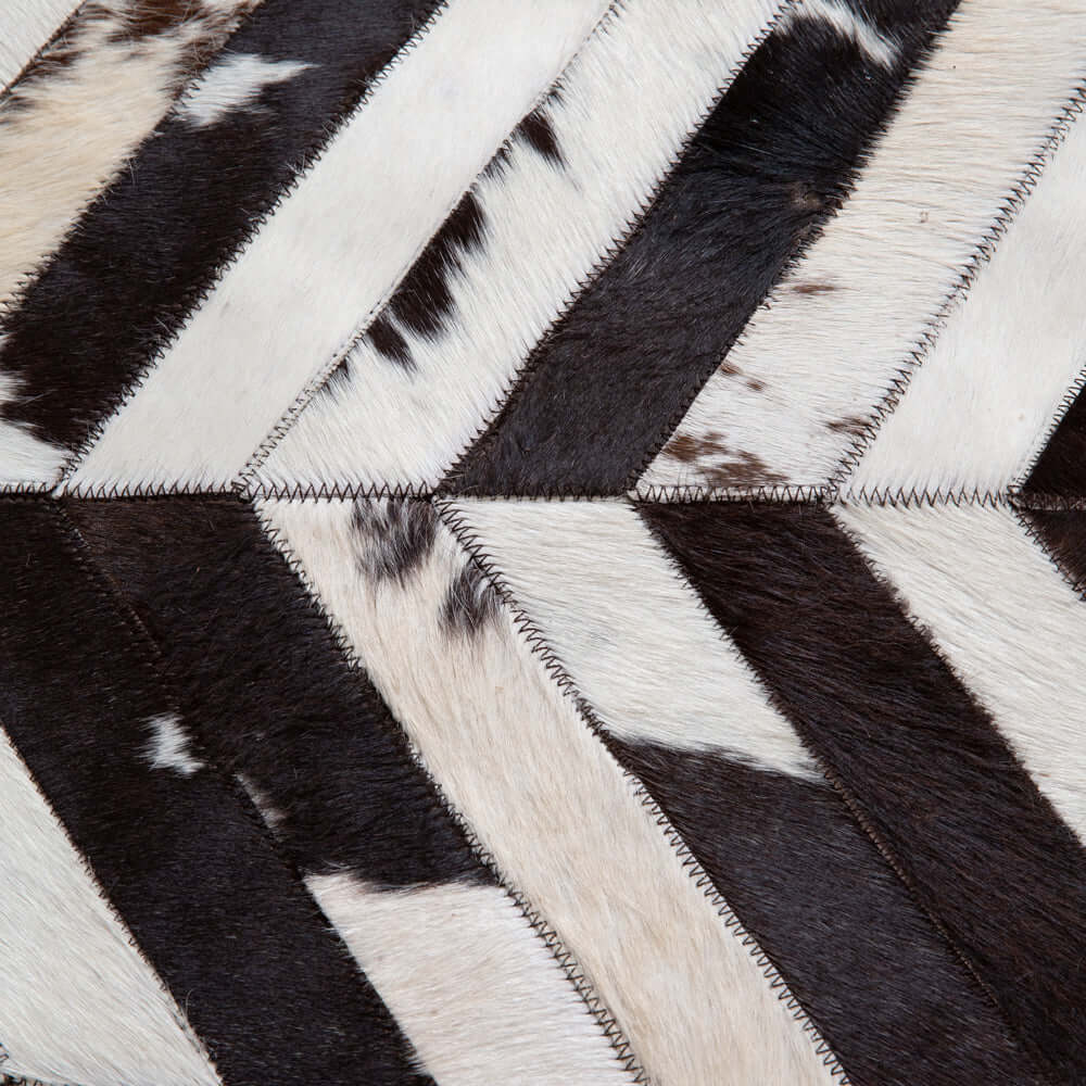 Close-up of vintage cowhide patchwork in chevron pattern with deep espresso, creamy ivory, and smoky charcoal tones.