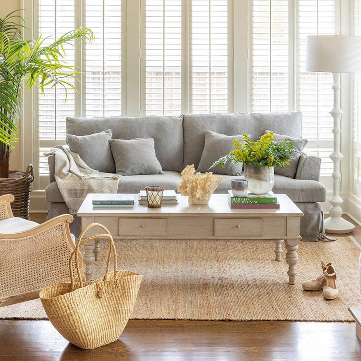 Vintage French Country Whitewashed Coffee Table With Drawers in cozy living room with gray sofa and decor items on tabletop.