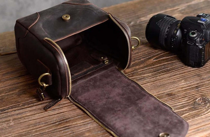 Vintage Full-Grain Leather Camera Bag "The Calista" open on wooden table with DSLR camera nearby.