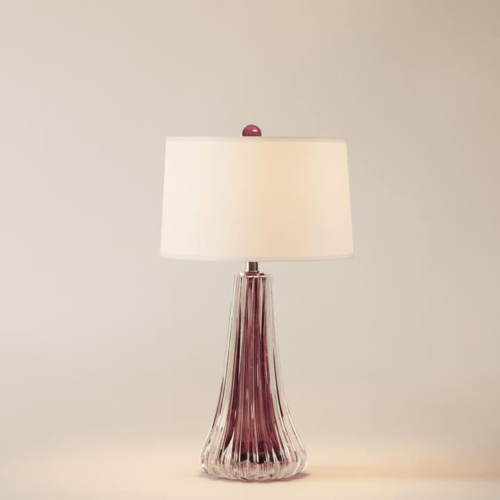 Table lamp with a purple glass base and white shade on a beige background