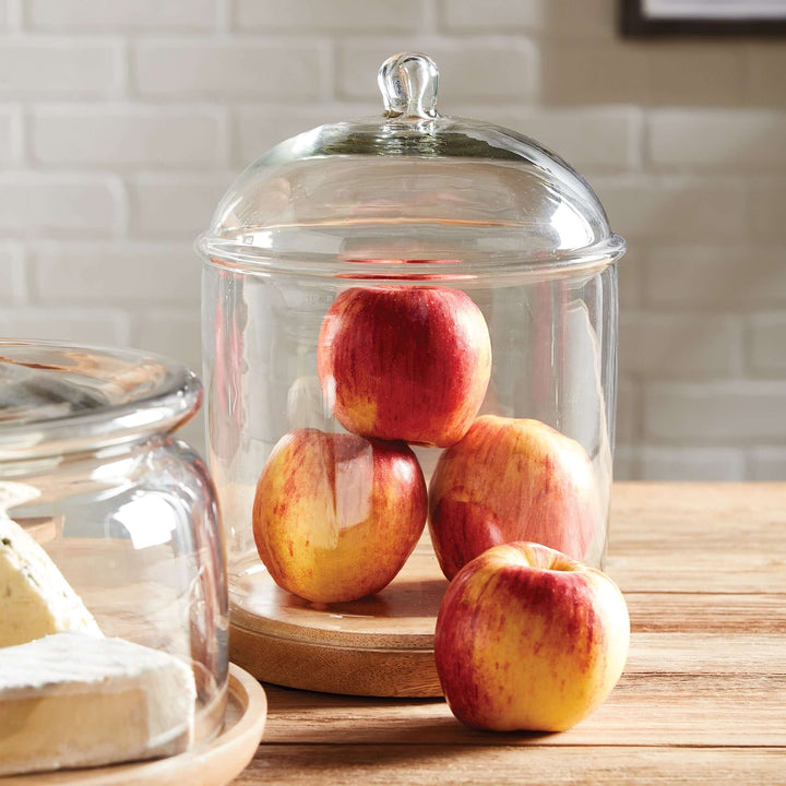 Vintage glass cloche with wood base displaying red apples, perfect for elegant kitchen decor.