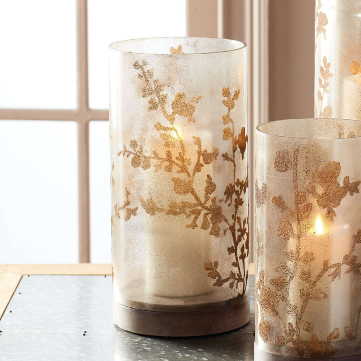 Vintage glass hurricane candle holder with botanical etching casting a warm glow.