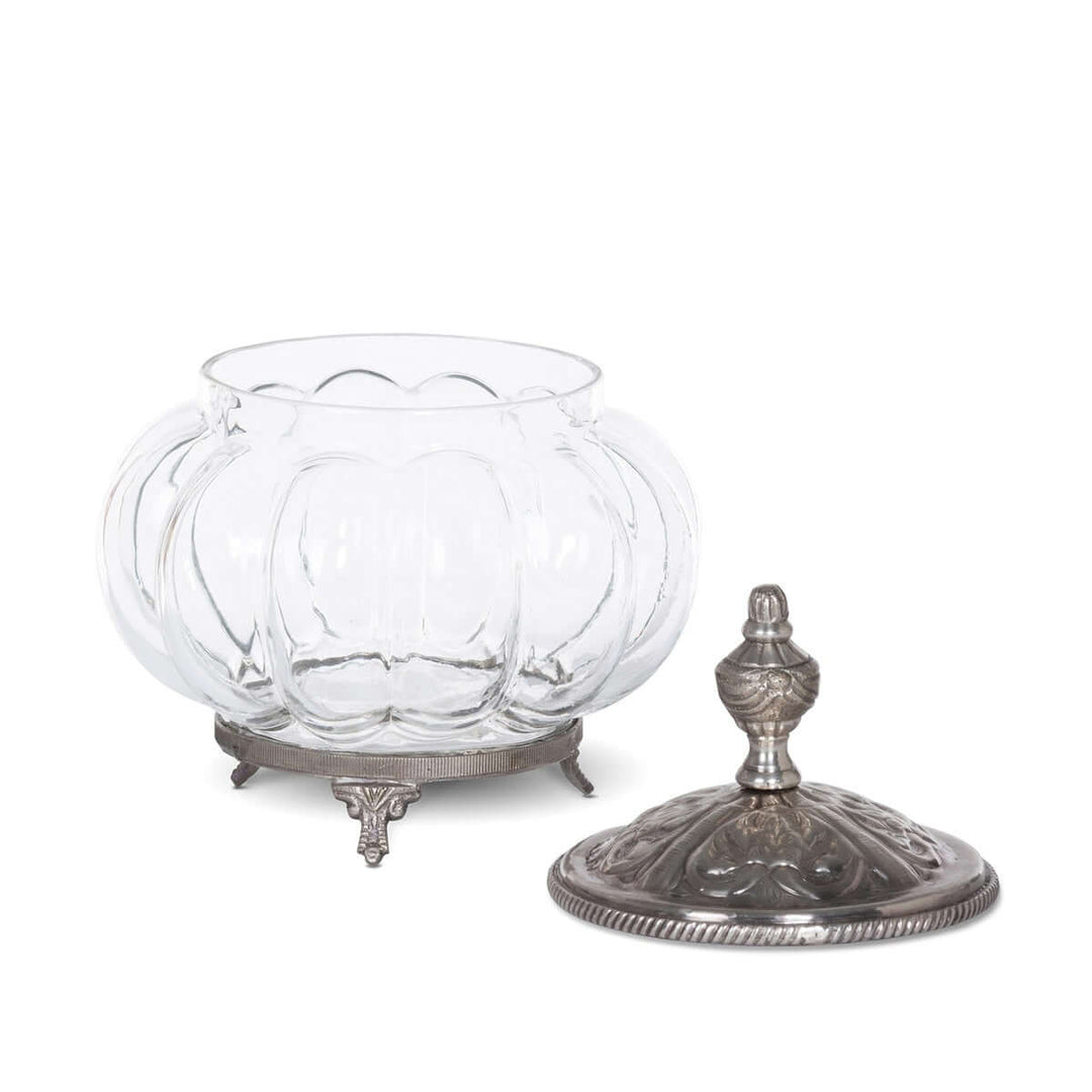Vintage glass vanity jar with ornate silver lid and decorative feet on white background.