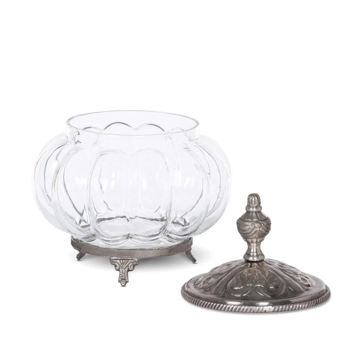 Vintage glass vanity jar with ornate silver lid and decorative feet on white background.