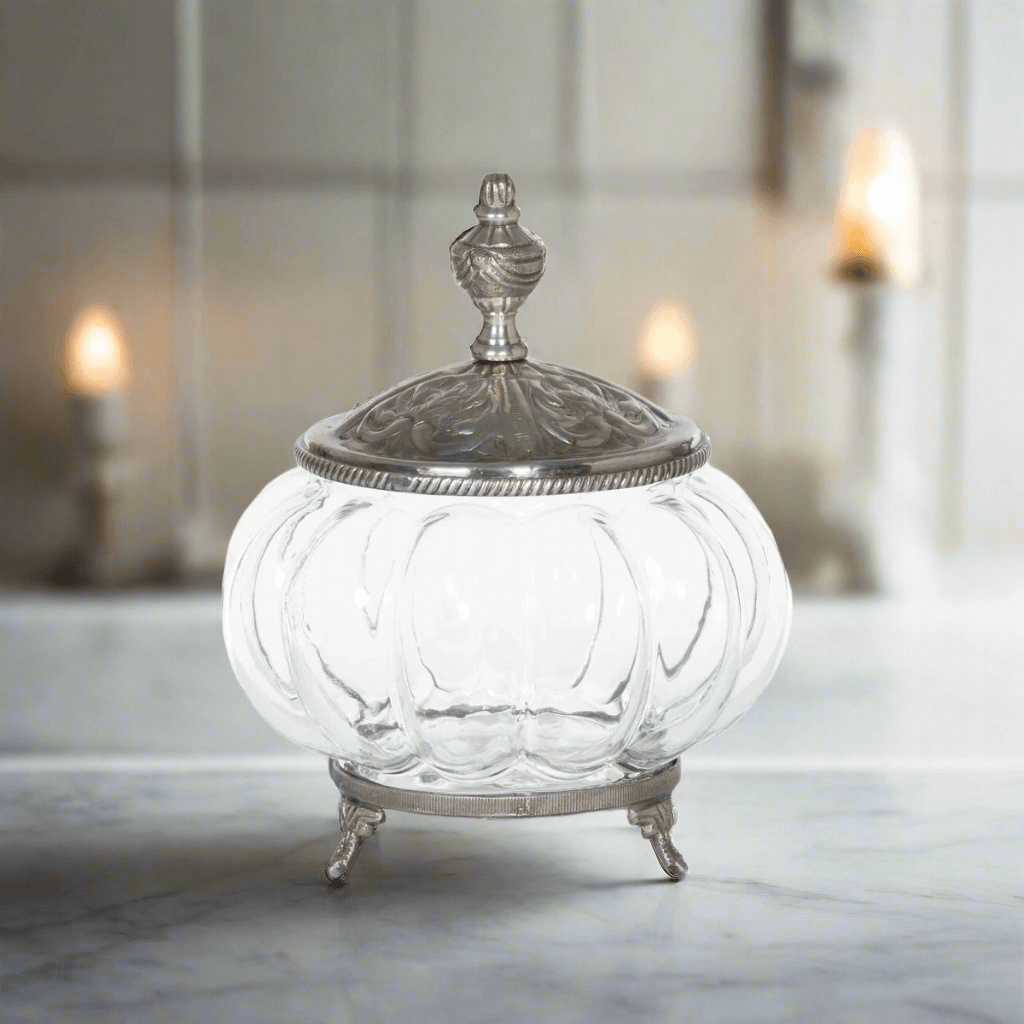 Vintage glass vanity jar with ornate silver lid on elegant marble table, embodying Victorian boudoir charm.