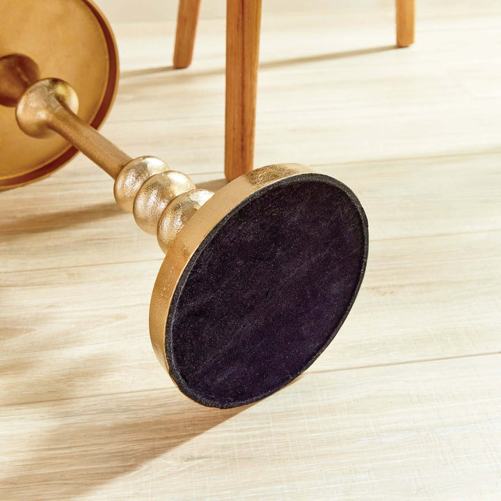 Close-up of the pedestal base of a vintage gold accent table showcasing its sculptural design and black felt bottom.