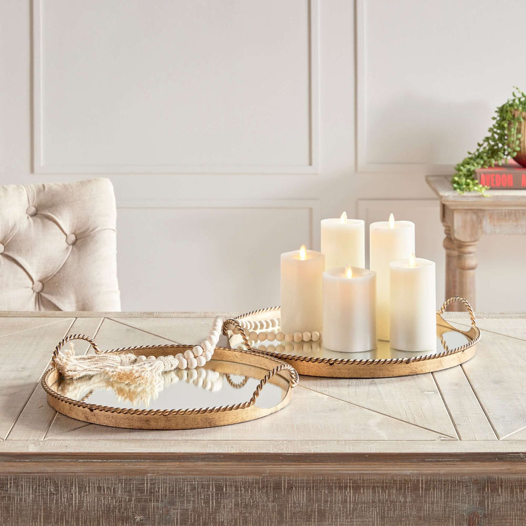 Vintage gold mirrored tray set with braided handles and candles on a wooden table.