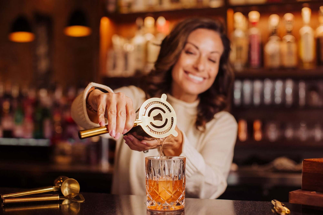 Woman using Vintage-Inspired Bar Tool Set with Brass Finish to make cocktail in elegant setting