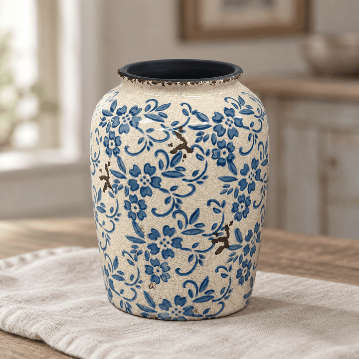 Close-up of a blue floral ceramic jar with a cream background and dark open rim on pale linen