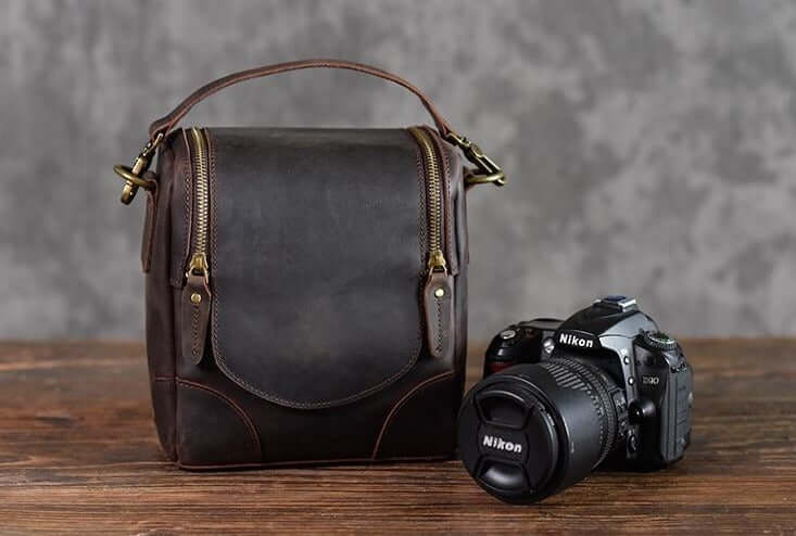 Vintage Full-Grain Leather Camera Bag "The Calista" beside a Nikon camera on a wooden table
