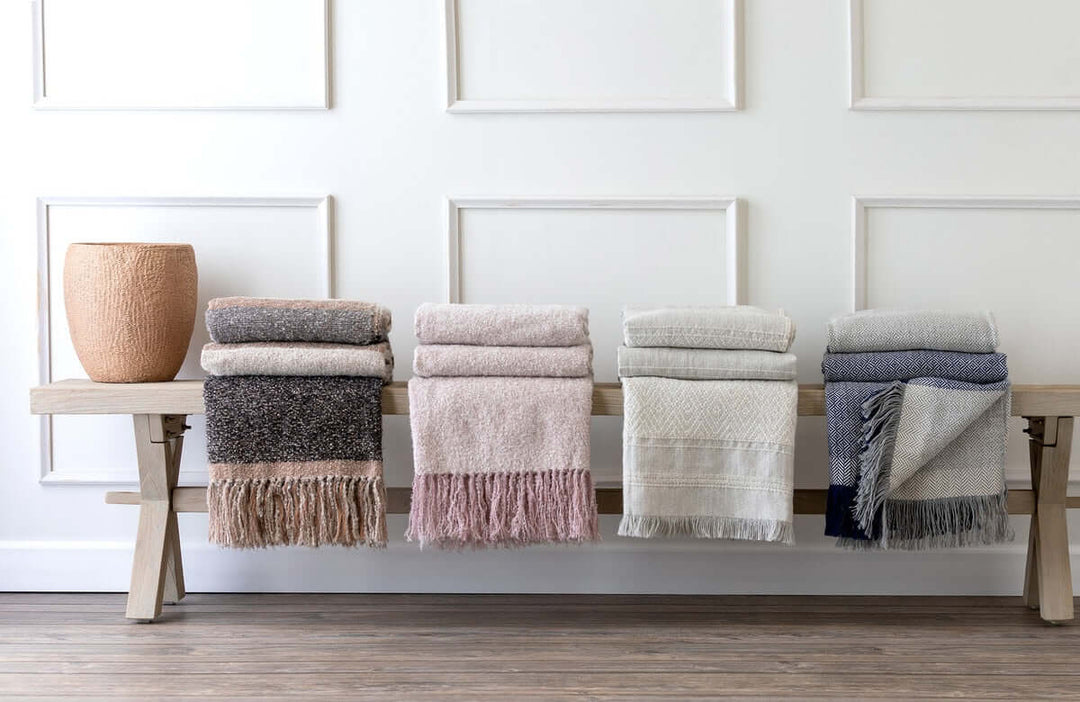 Vintage Light Blush Boucle Alpaca Wool Throw Blanket displayed on a wooden bench with other soft woven blankets.