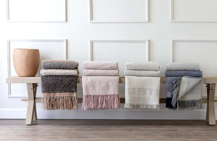 Vintage Light Blush Boucle Alpaca Wool Throw Blanket displayed on a wooden bench with other soft woven blankets.