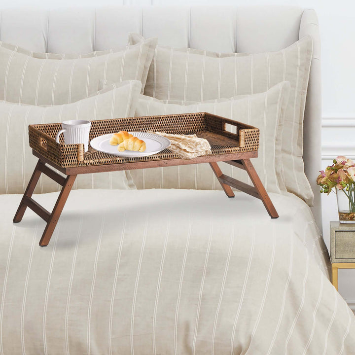 Vintage rattan tray table with collapsible legs, featuring a breakfast setup on a bed with elegant linens.
